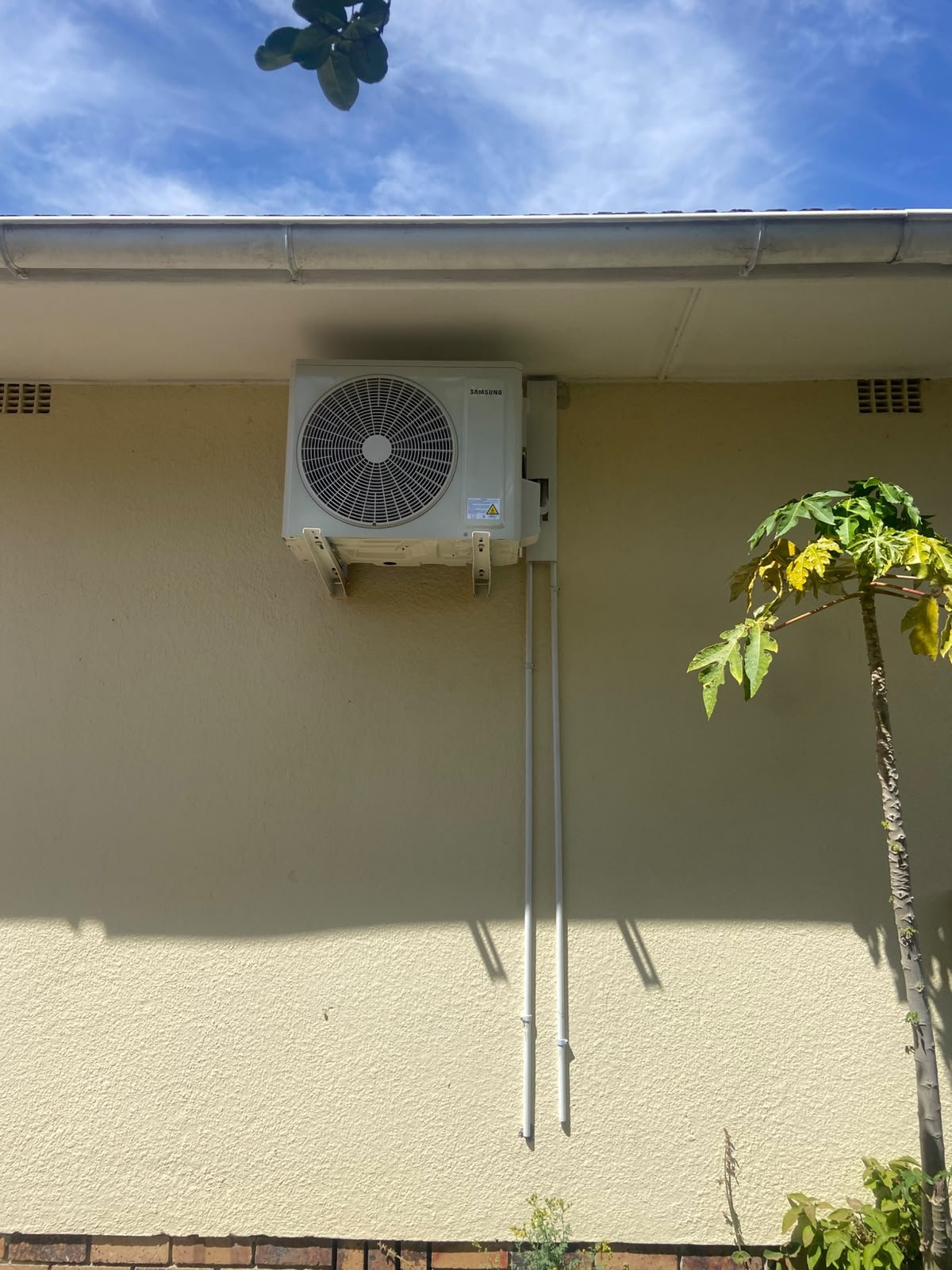 Aircon outdoor unit wall-mounted under the eaves with neat pipe runs, installed by Mount-IT